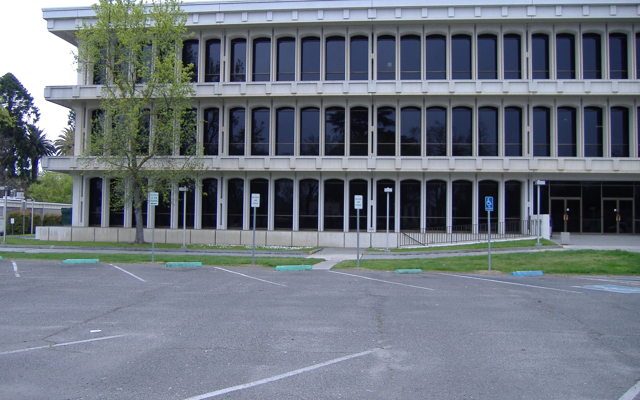 The Merced County Administration Building, a three-story concrete office building with tall arched windows, seen across a parking lot.